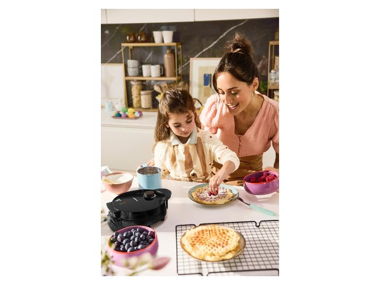 Moeder en dochter versieren wafels met bessen en bosbessen, naast een wafelijzer.