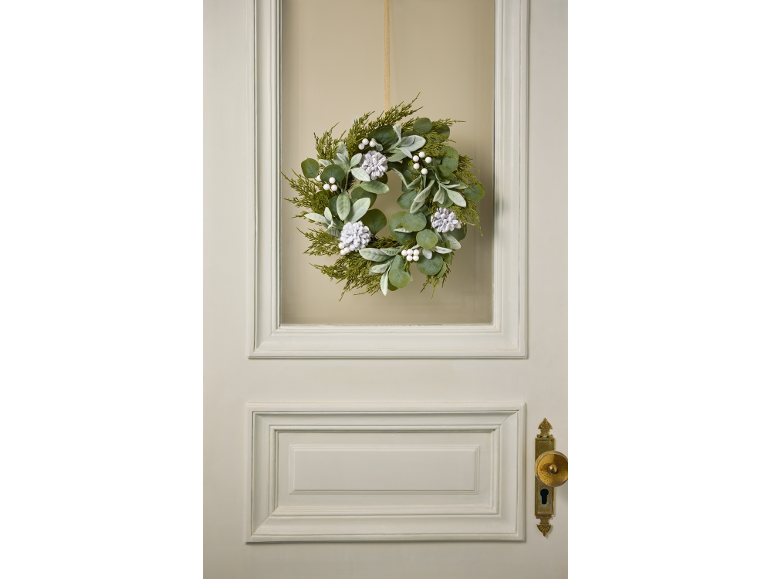 Winterkrans met groen blad, witte bessen en dennenappels aan een deur.