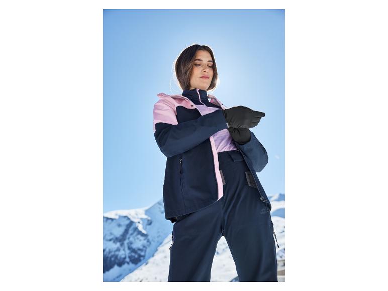 Vrouw in ski-jas en -broek, handschoenen aanpassend op een zonnige piste.