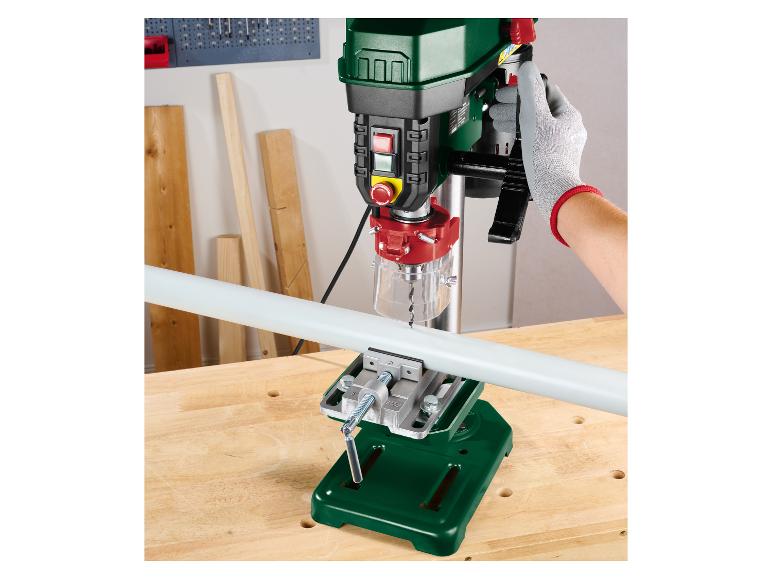 Parkside kolomboormachine boort een pijp vastgezet met een bankschroef op een houten werkbank.