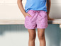 Een kind draagt roze shorts met schelpenprint.