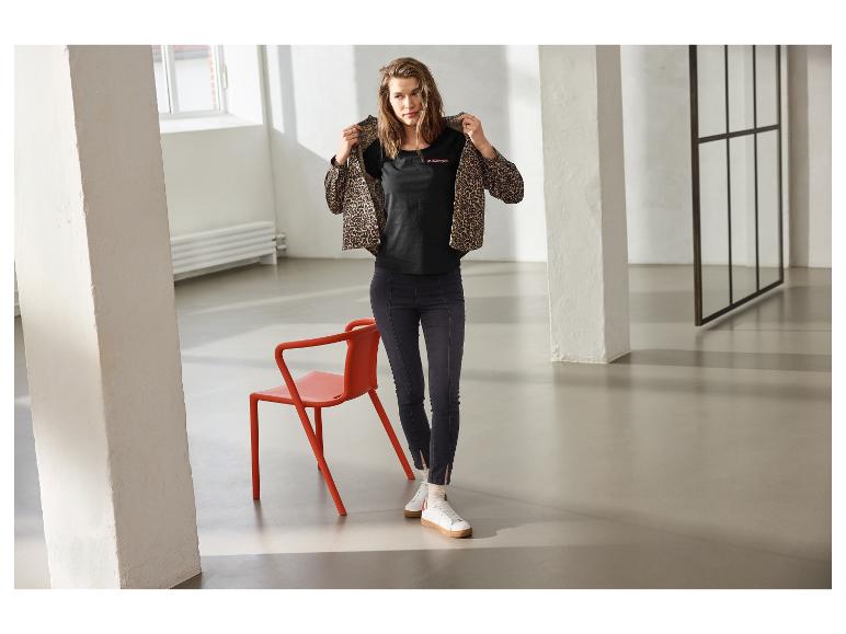 Vrouw in donkere ESMARA jeggings, zwart T-shirt en luipaardjas.