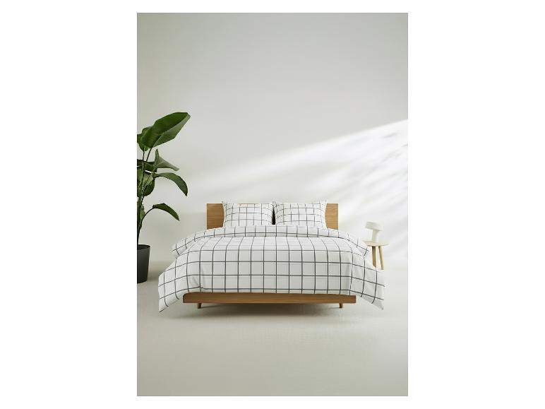 Bed met wit en zwart geruit beddengoed, groene plant en nachtkastje met lamp.