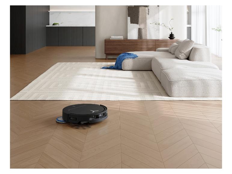 Robotstofzuiger reinigt houten vloer in moderne woonkamer met bank en vloerkleed.