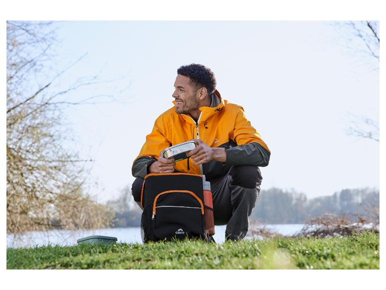 Man in oranje Crivit jas pakt lunch in bij een meer.