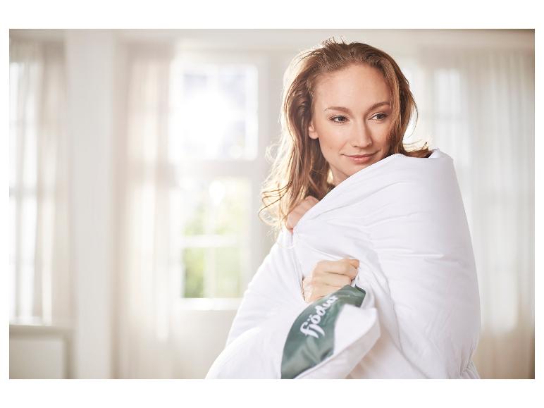 Een vrouw gewikkeld in een wit Fjödur-dekbed in een lichte kamer.