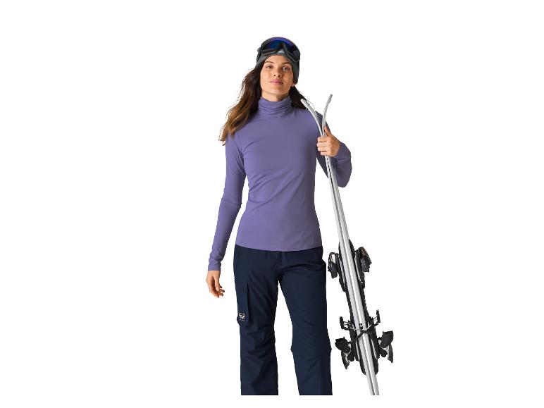 Vrouw in paarse coltrui en donkere broek met ski's.