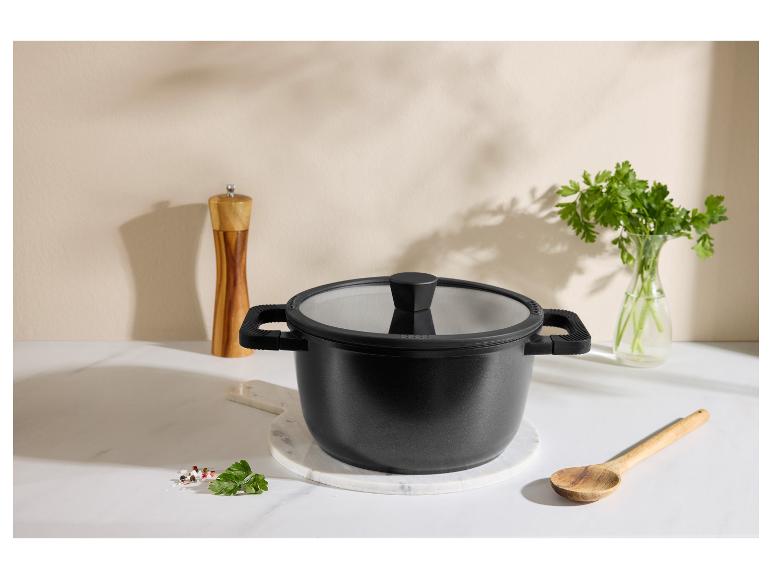 Zwarte kookpot met deksel, houten lepel, pepermolen en peterselie op een aanrecht.