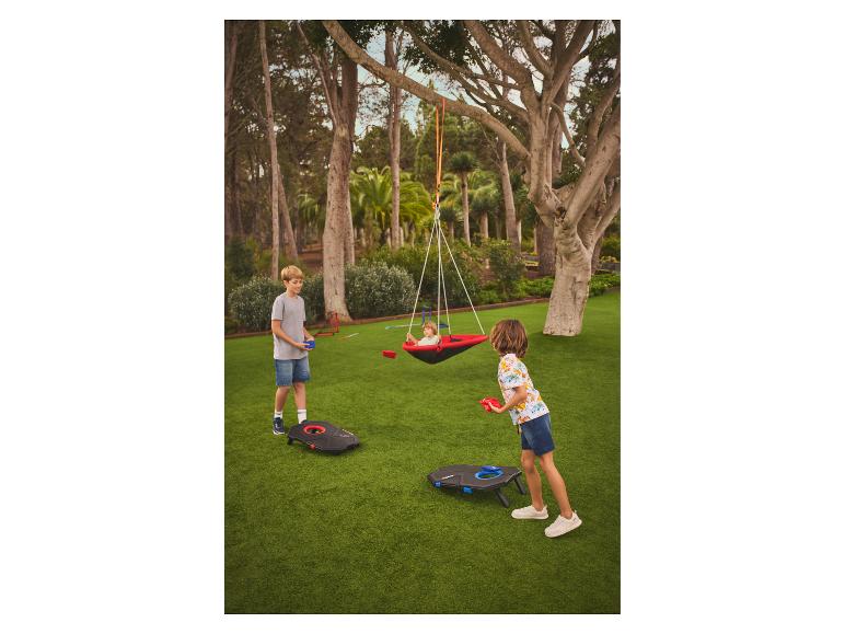 Kinderen spelen met een zitzakwerpspel en een schommel in een tuin.