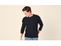 Man in een zwart henley-shirt met lange mouwen en jeans, kijkt naar beneden.