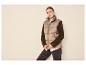 Vrouw in beige puffer bodywarmer, wit overhemd en donkere jeans.