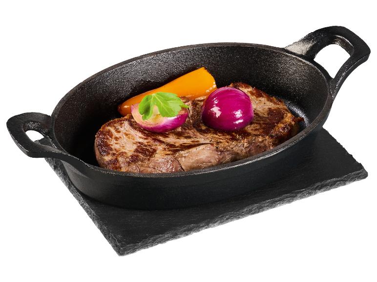 Biefstuk met rode ui en paprika in een gietijzeren pan op een stenen plank.