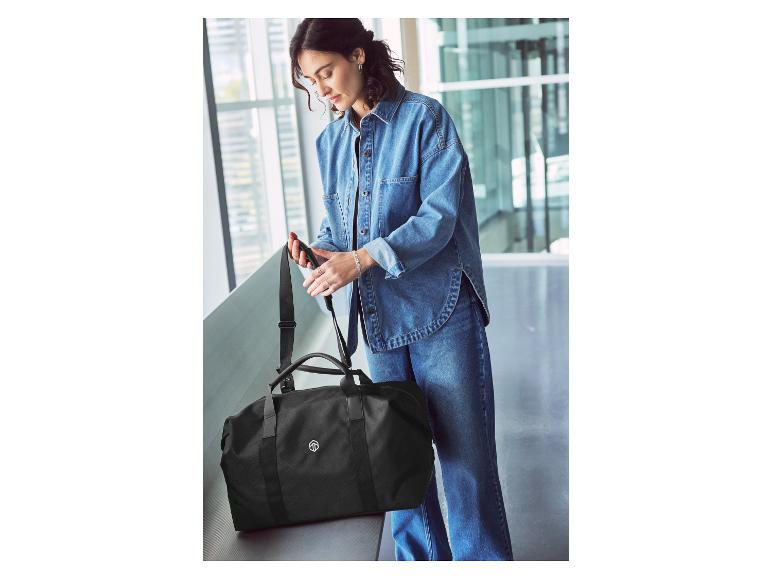 Een vrouw in een spijkerjasje inspecteert een zwarte reistas.