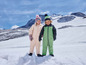 Twee kinderen in wintersportkleding staan in de sneeuw.