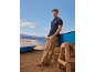 Man in marineblauwe polo en beige broek op het strand met boten.