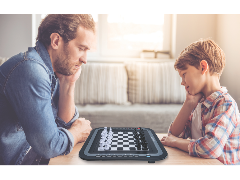 Een vader en zoon spelen op een elektronisch schaakbord aan een houten tafel.