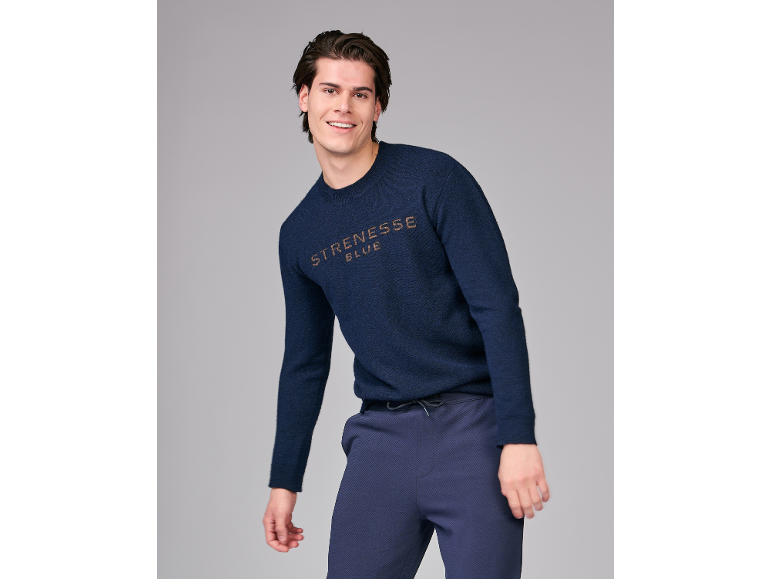 Een glimlachende man in een donkerblauwe gebreide trui en bijpassende broek.