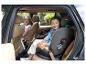 Twee kinderen in autostoeltjes achterin een auto, één lacht naar de camera.
