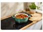 Een groene Le Creuset pan met stoofpot op een inductiekookplaat.