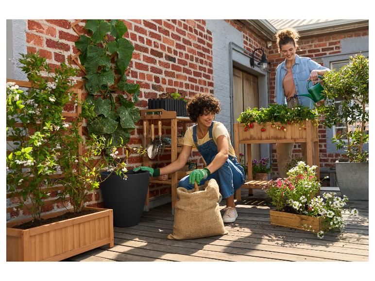 Twee vrouwen tuinieren op een balkon met houten plantenbakken en tuingereedschap.
