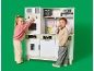 Twee kinderen spelen met een grote houten speelgoedkeuken tegen een groene achtergrond.