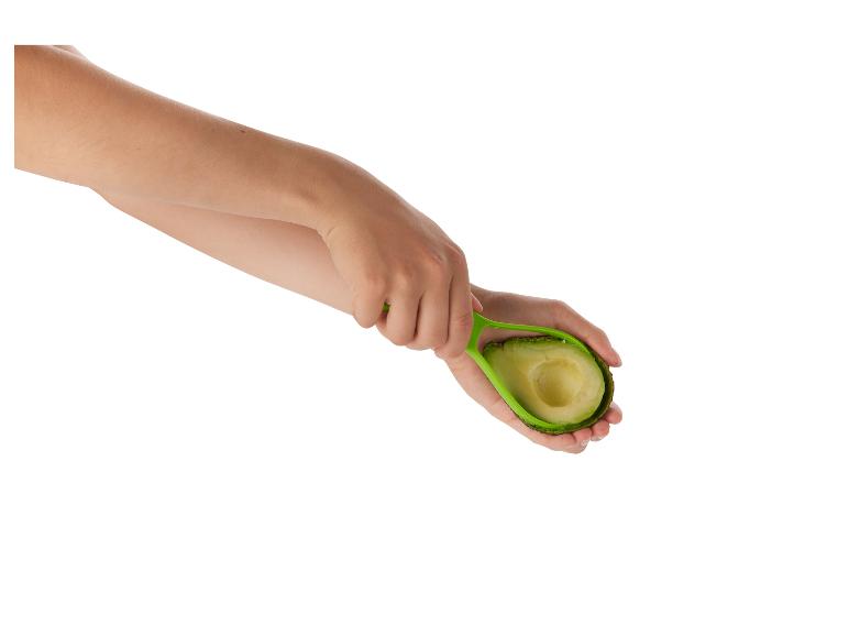 Een vrouw houdt een avocado vast en een groene tool om hem te schillen.