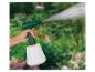 Handtuinspuit met verneveld water, vastgehouden door een persoon tegen een groene achtergrond.