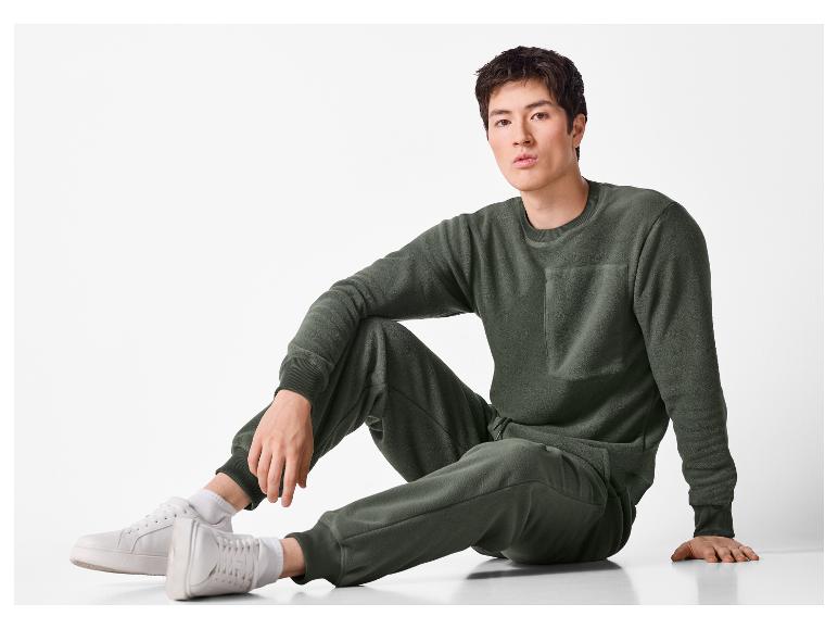 Man in een donkergroene fleece sweater en joggingbroek zit op de grond.