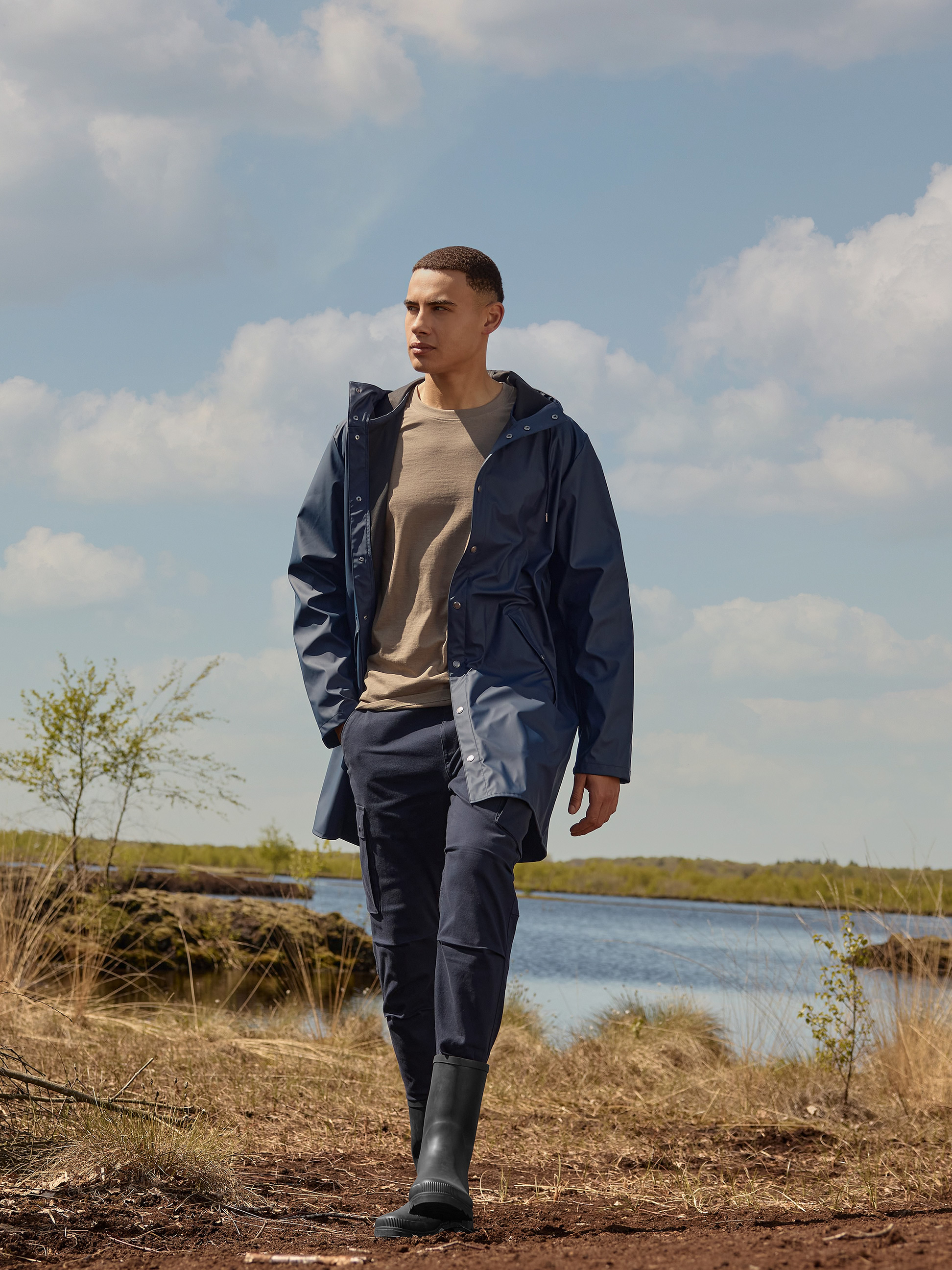 Donkerblauwe regenjas en broek voor heren, bruin T-shirt, zwarte regenlaarzen in de natuur.