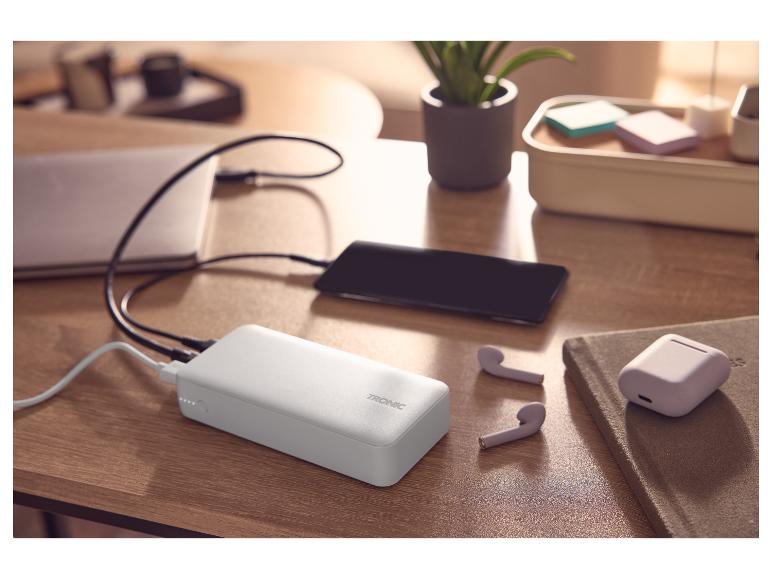 Powerbank laadt telefoon en laptop op, met draadloze oordopjes op een bureau.