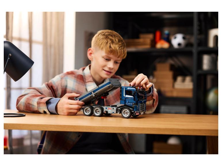 Een jongen monteert een blauwe speelgoedtruck op een houten tafel.