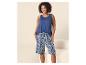 Vrouw in een blauwe tanktop en een blauw-wit gestreepte korte broek, lachend.