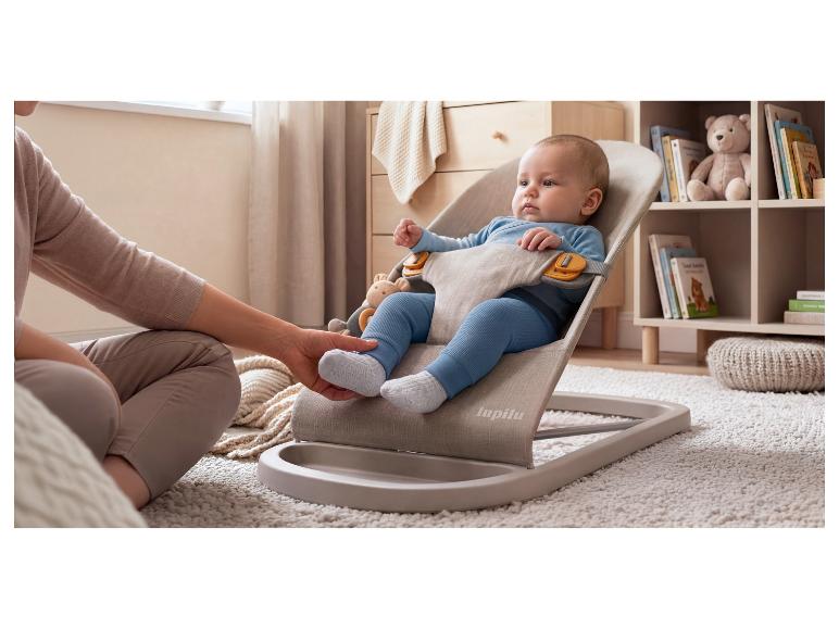 Baby in een wipstoel, met de hand van een volwassene die de voet van de baby aanraakt, op een pluizig tapijt.