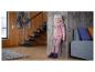 Lachend meisje in roze trui en broek, met schoenen aan, leunend tegen een houten muur.