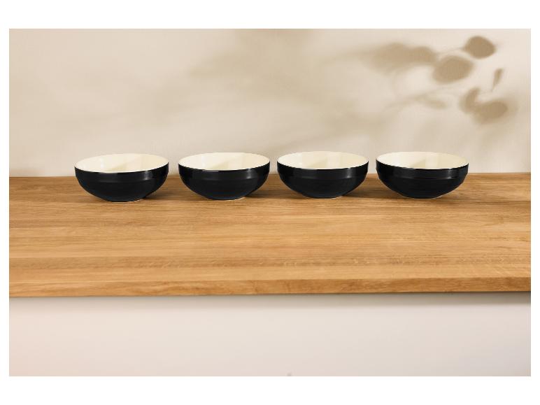 Vier zwarte kommen op een lichte houten tafel, met bladschaduwen op de muur.