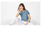 Vrouw in blauw geborduurd T-shirt en witte broek, zittend.