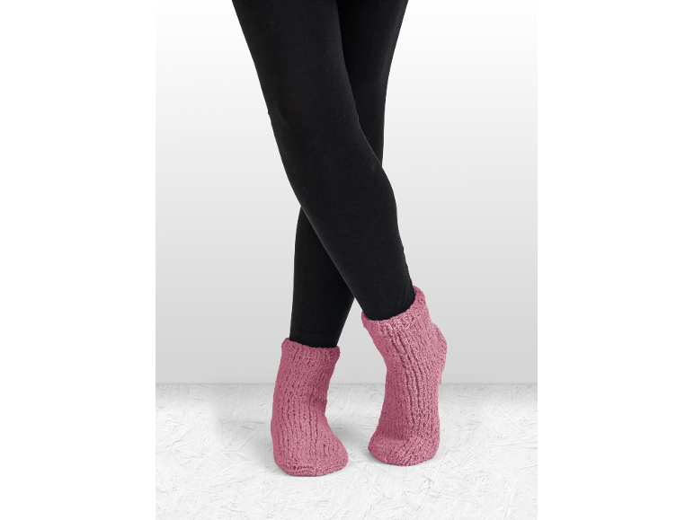 Benen in zwarte leggings en roze gebreide pantoffelsokken.