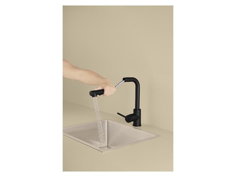 Hand houdt zwarte keukenkraan met uittrekbare sproeikop boven een roestvrijstalen spoelbak.
