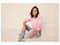 Vrouw zit in roze trui en jeans, lachend naar de camera.