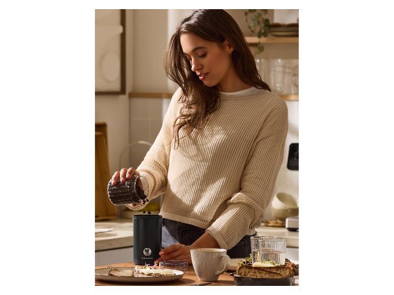 Vrouw giet koffiebonen in een SilverCrest koffiemolen op een aanrecht.