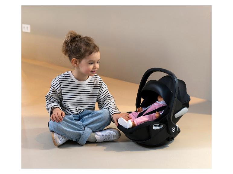 Een klein meisje met een gestreept truitje zit naast een Cybex babyautostoeltje.