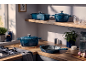 Blauwe gietijzeren kookpannen en koekenpannen op een houten keukenwerkblad.