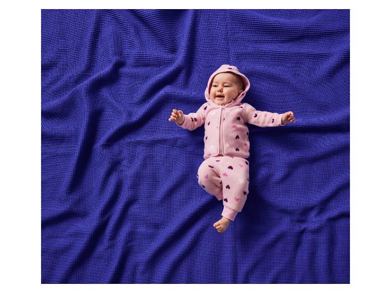 Blije baby in een roze pakje met hartjes, liggend op een blauwe deken