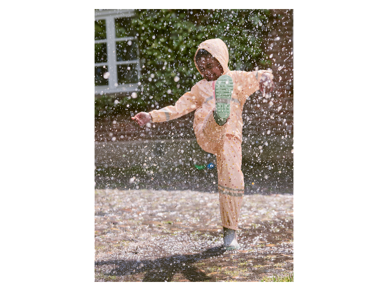 Meisje speelt in een plas met regenkleding.