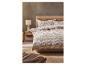 Een moderne slaapkamer met een houten bedframe, beddengoed met patroon en een bedlampje.