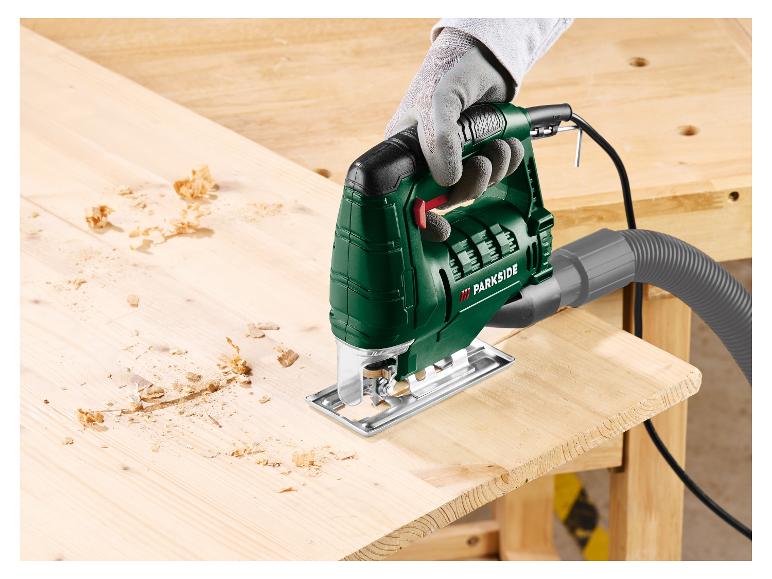 Groene Parkside decoupeerzaag zaagt een houten plank, met zaagsel.