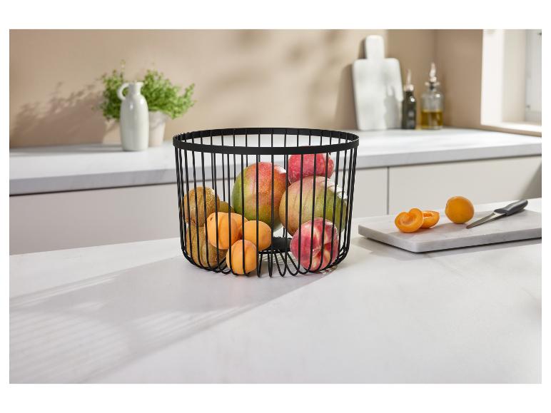 Zwarte draad fruitmand gevuld met mango's, kiwi's, perziken en abrikozen op een aanrecht.