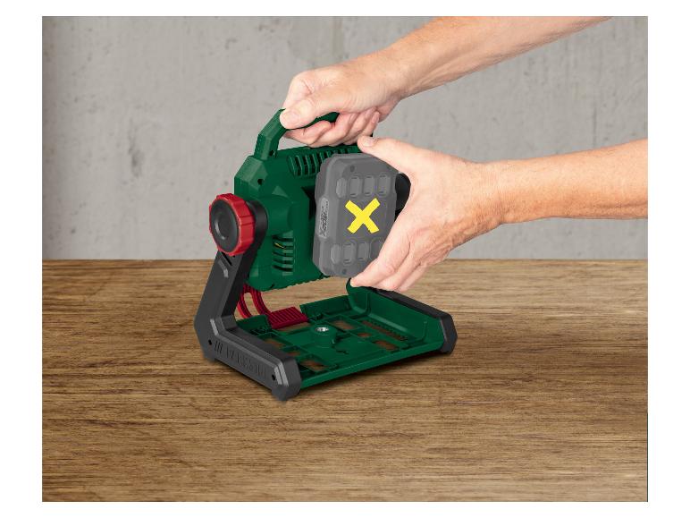 Handen plaatsen een grijze accu met een gele X in een groen-zwarte werklamp.