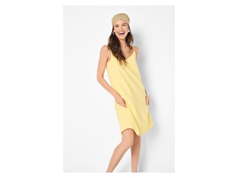 Vrouw in gele spaghettibandjesjurk met hoofddoek, lachend.