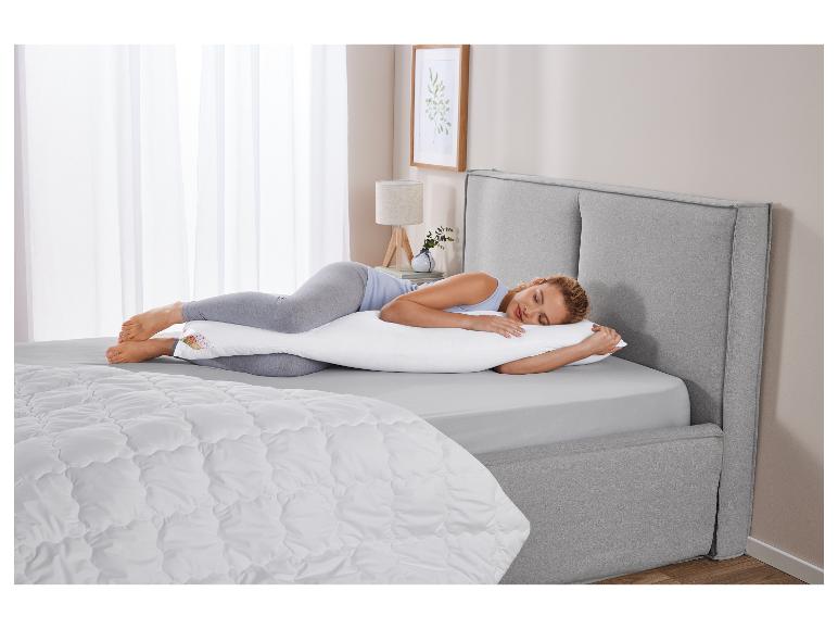 Een vrouw slaapt rustig in een bed met een zwangerschapskussen.